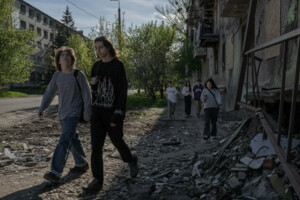 Денис (ліворуч) та Микита проходять повз зруйнований снарядами житловий будинок, а їхні друзі слідують за ними